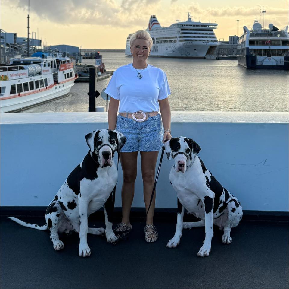 Sarah Tempest with two great dane dogs on a boat deck with ships in the background