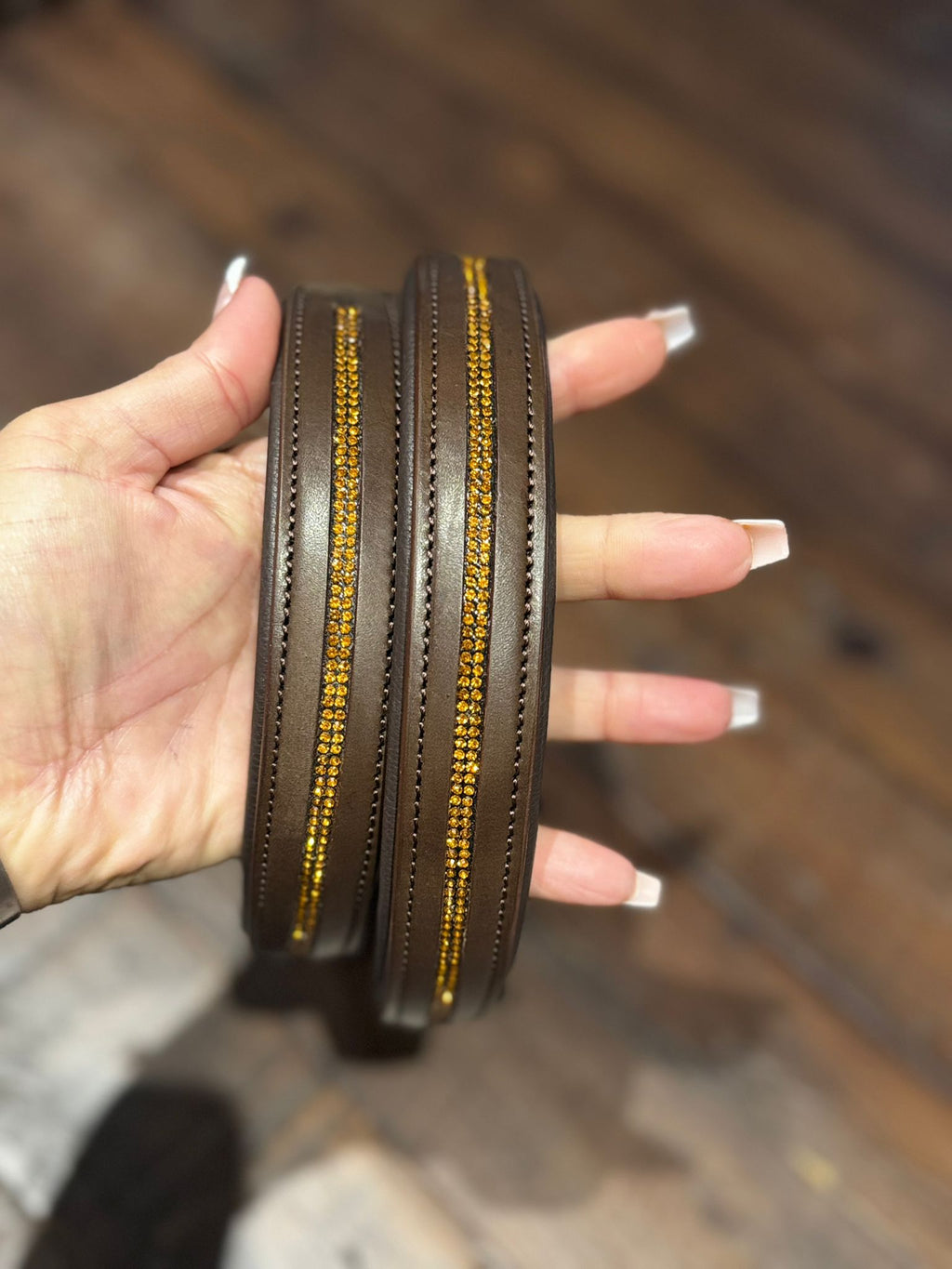 A hand holding a brown leather figure of 8 head collar, embellished with handcrafted gold rhinestones