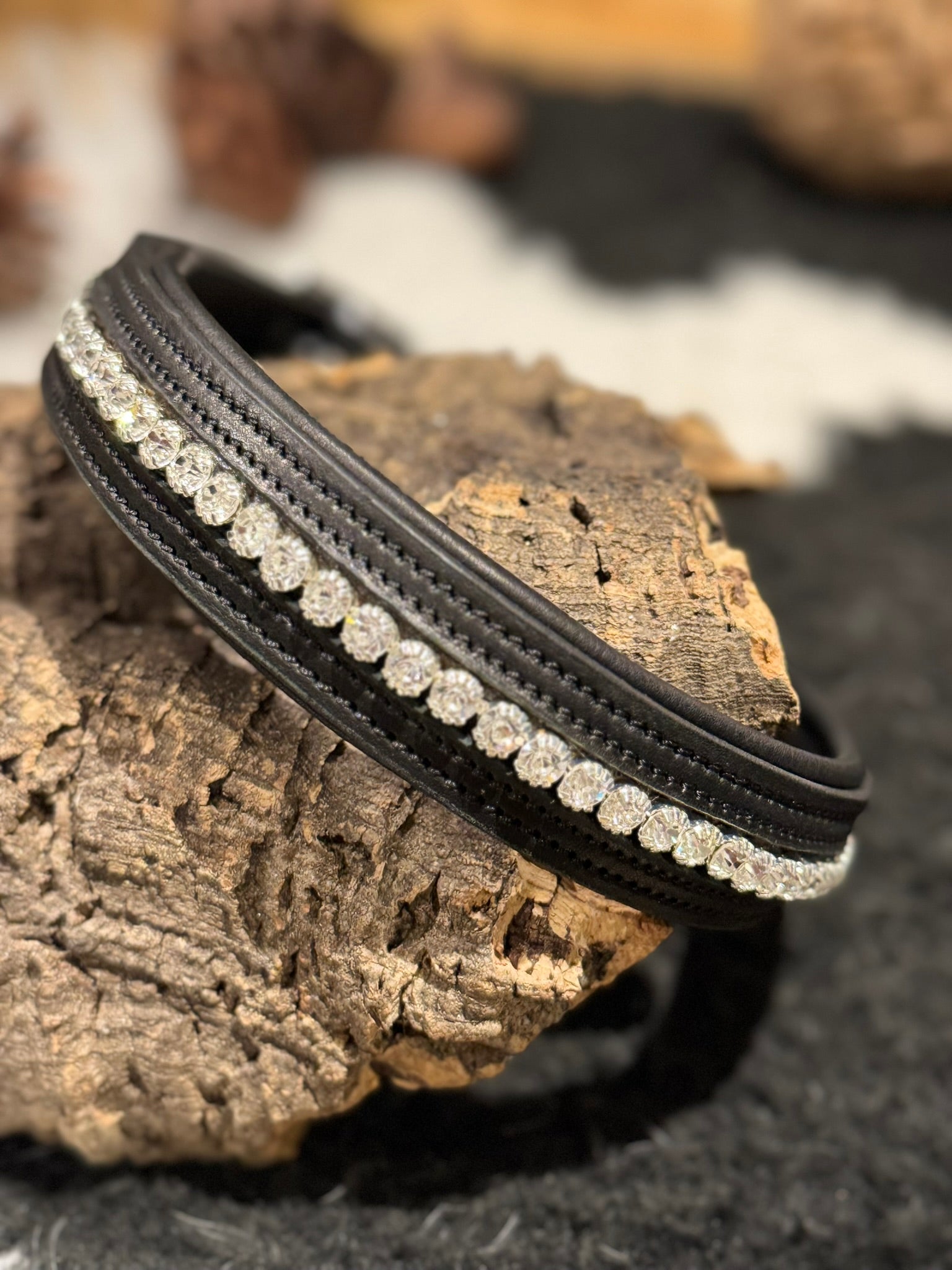 Black leather bracelet with clear crystal studs on a wooden surface